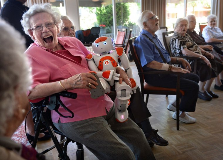 Oudere vrouw lacht met zorgrobot in de armen.
