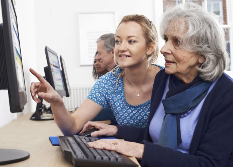 Vrouw legt iets uit aan oudere vrouw achter de computer