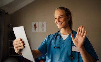Verpleegkundige zwaait naar tablet waarop ze beeldbelt met patiënt