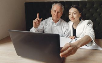 Oudere man en jonge vrouw zitten samen te beeldbellen achter een laptop.