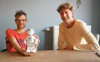 Cliënt Rick houdt robot Maatje vast en naast hem zit coördinator innovatie Martijn Schep.