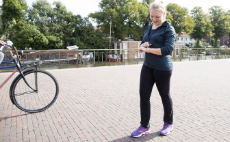 Vrouw in sportoutfit kijkt op smartwatch tijdens het lopen.