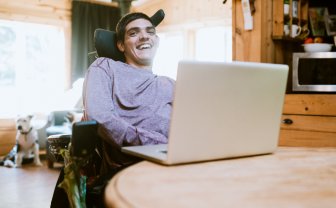 Vrolijke jongeman in rolstoel gebruikt laptop met oogbesturing