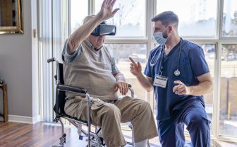Oudere man met VR bril beweegt zijn arm terwijl hij wordt begeleid door een zorgmedewerker