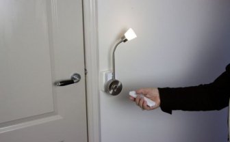 Een hand heeft een afstandsbediening vast en richt deze op een lamp aan de muur.