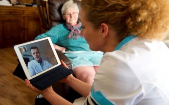 Zorgverlener bij patiënt thuis en overlegt met een collega via een tablet.
