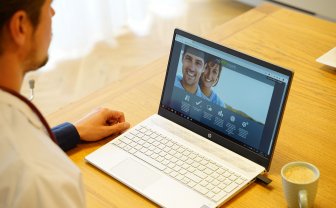 Een man zit achter een laptop die op tafel staat. Op het scherm van de laptop is MijnIBDcoach te zien.