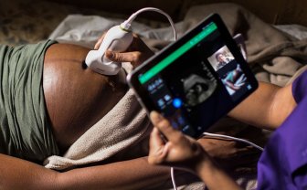 Een zwangere vrouw ligt op de behandeltafel en er wordt een echo gemaakt op een tablet