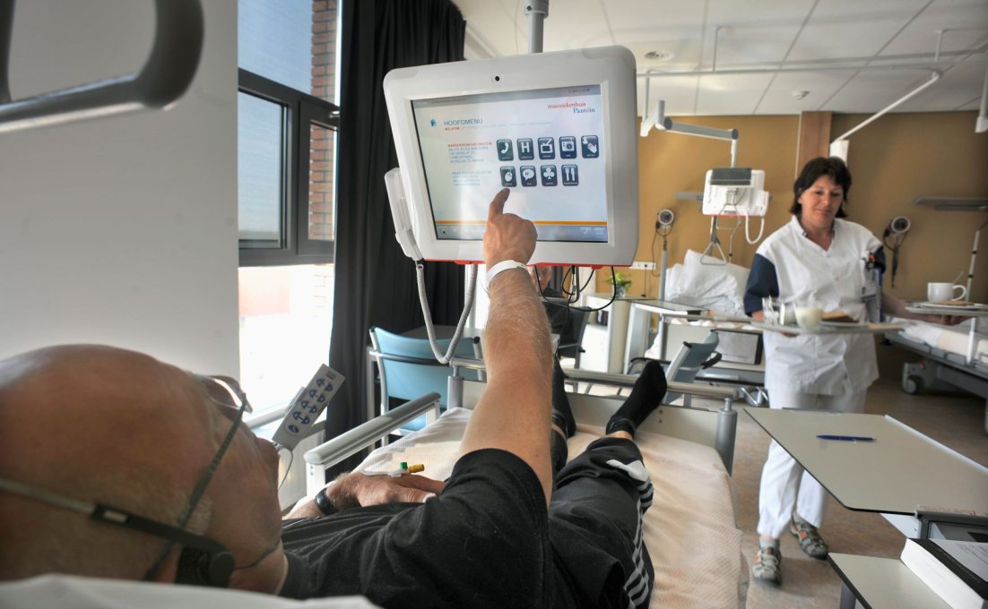 Man in ziekenhuisbed tikt iets aan op het scherm dat aan zijn bed vastzit.