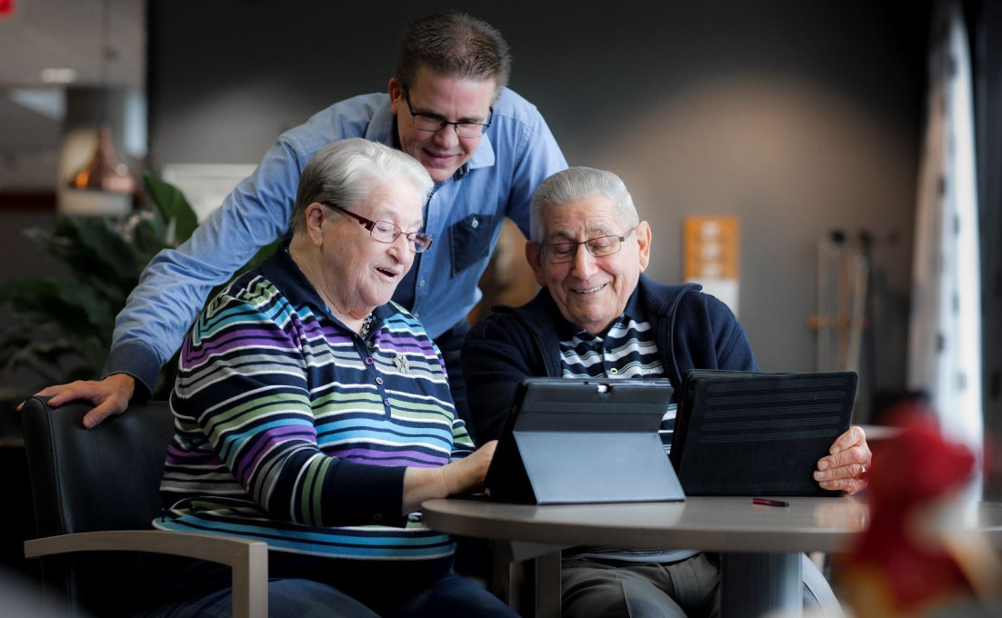 Drie ouderen kijken geamuseerd naar een tablet.