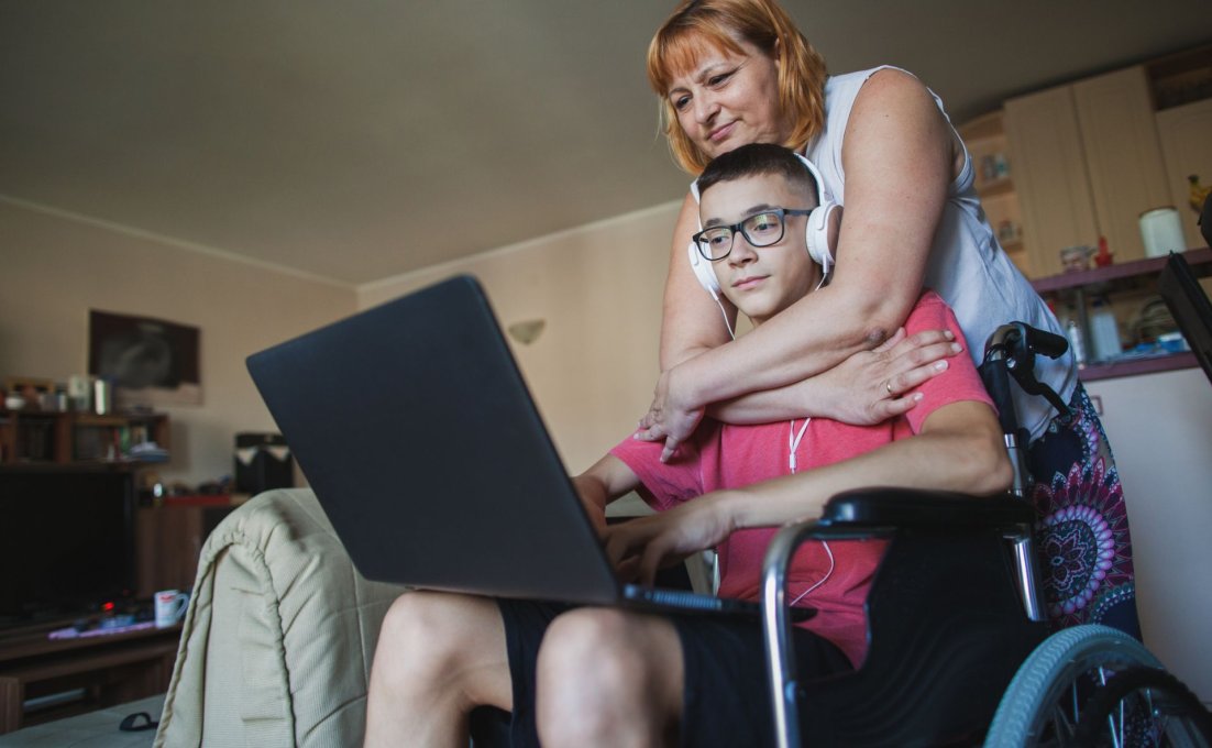 Moeder heeft armen geslagen om zoon in rolstoel met laptop op schoot