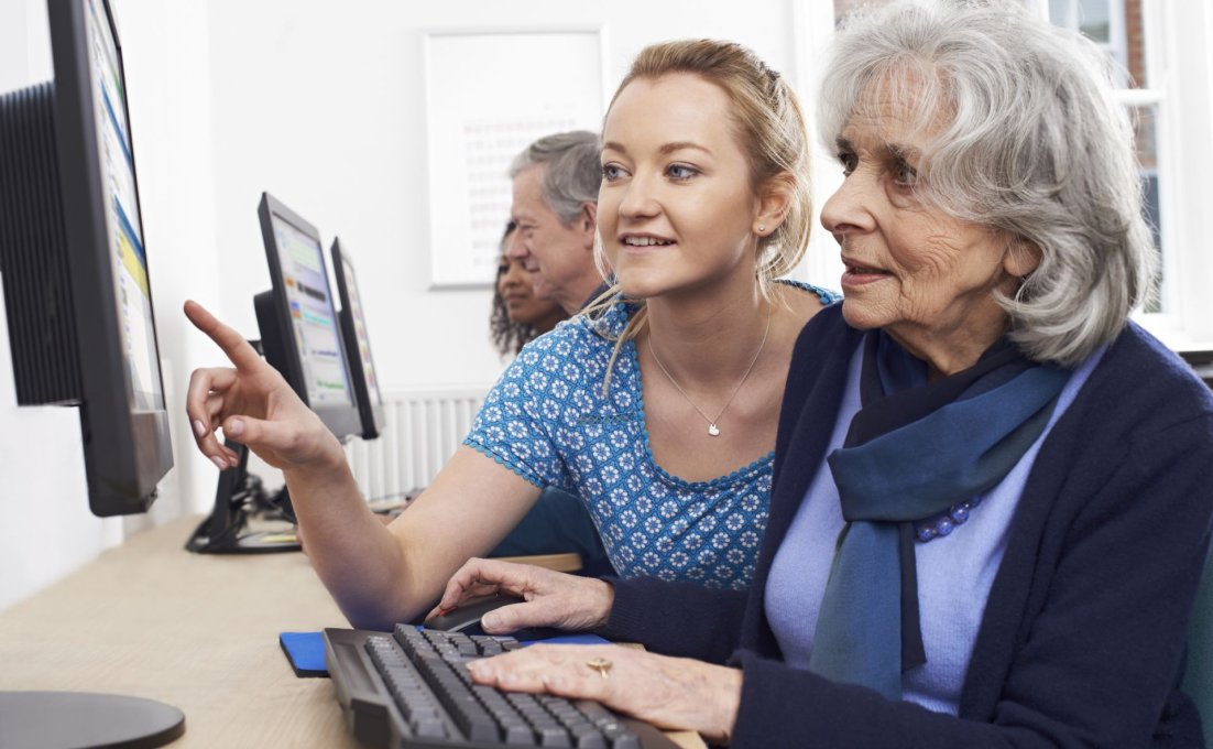 Vrouw legt iets uit aan oudere vrouw achter de computer
