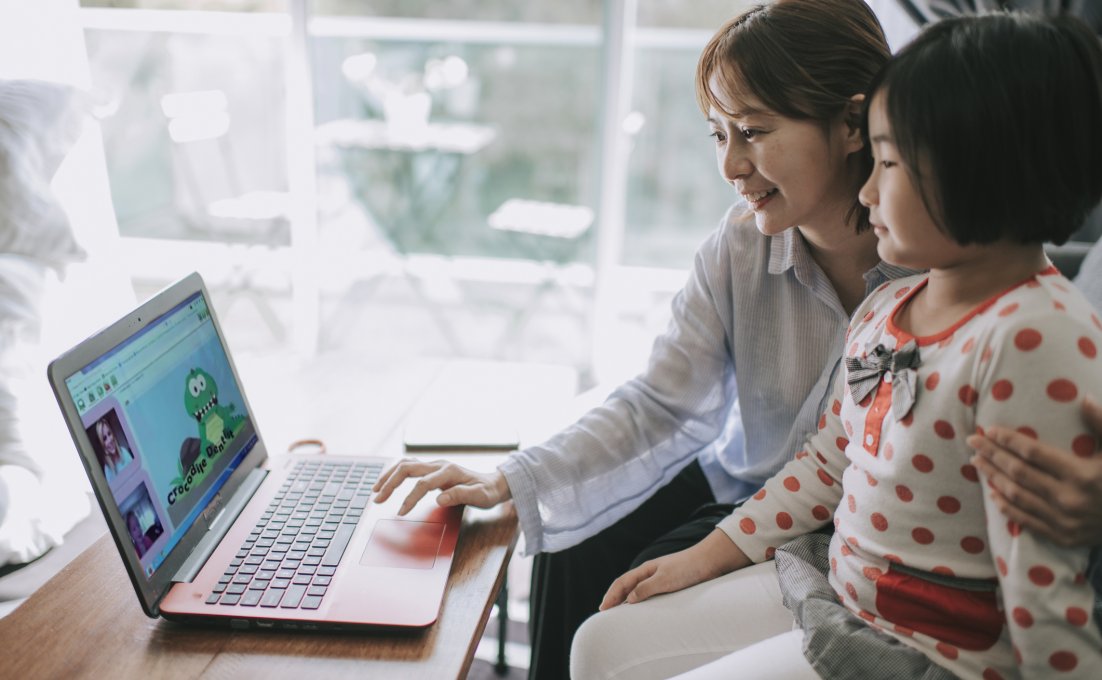 Moeder en dochter kijken samen naar laptop met daarop online logopedie spel