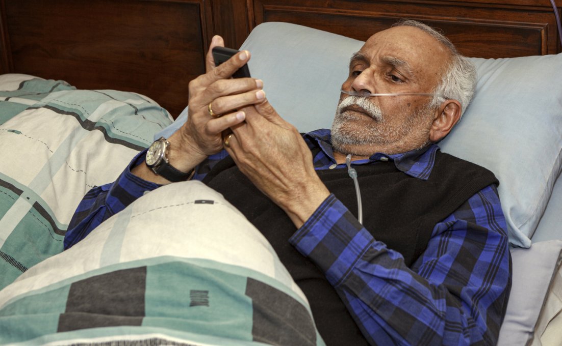 Man herstellend van operatie thuis in zijn bed met smartphone in zijn handen