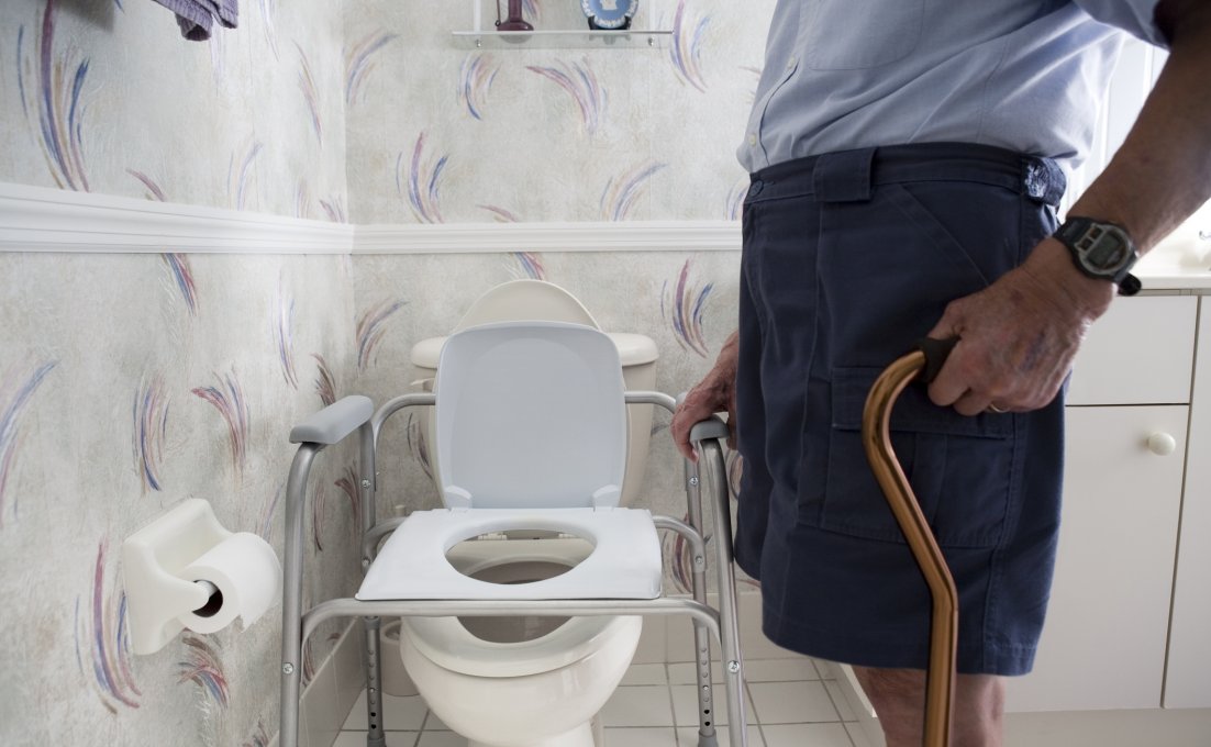 Oudere man staat bij toilet met daarop een hulpmiddel om makkelijker van het toilet af te komen