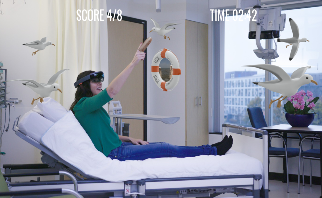 Een vrouw op een ziekenhuisbed speelt het spel Fitte Vogels. met een VR-bril. Hologrammen van vogels zijn zichtbaar in de kamer 