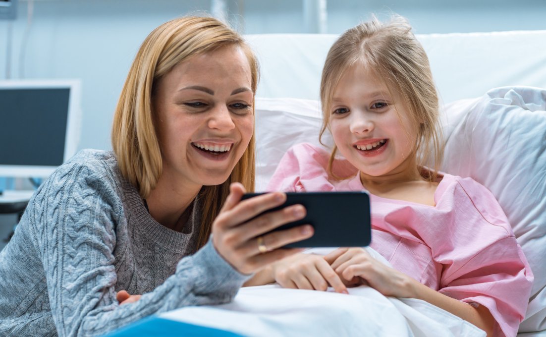 Kind in ziekenhuis bed kijkt met moeder mee op smartphone