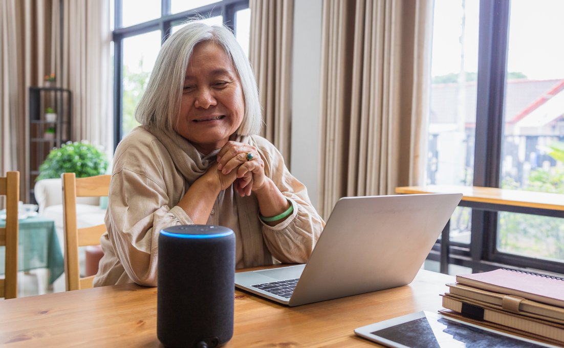 Oudere vrouw met laptop kijkt naar spraakassistent