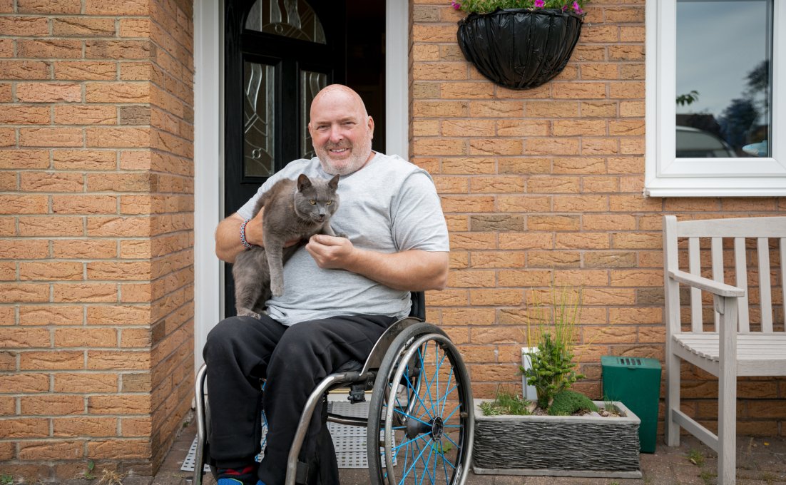 Man in rolstoel voor zijn huis met drempelhulp