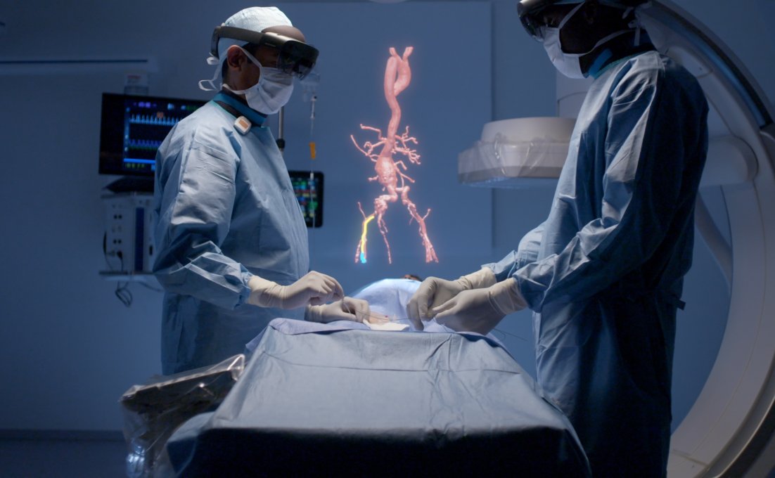 Twee chirurgen voeren een operatie uit. Beiden dragen een HoloLens 2 bril. Er zweeft een virtuele afbeelding van een bloedvat.