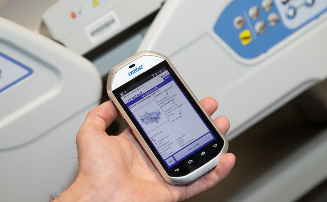 Zorgprofessional met smart phone in zijn hand waarop de app CureTrack te zien is, track and trace voor medische apparatuur